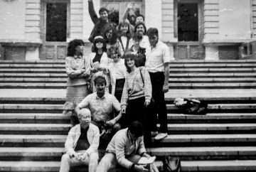 A black-and-white group photo shows several people gathered on outdoor steps in front of a large building, with one person with albinism seated near the front.